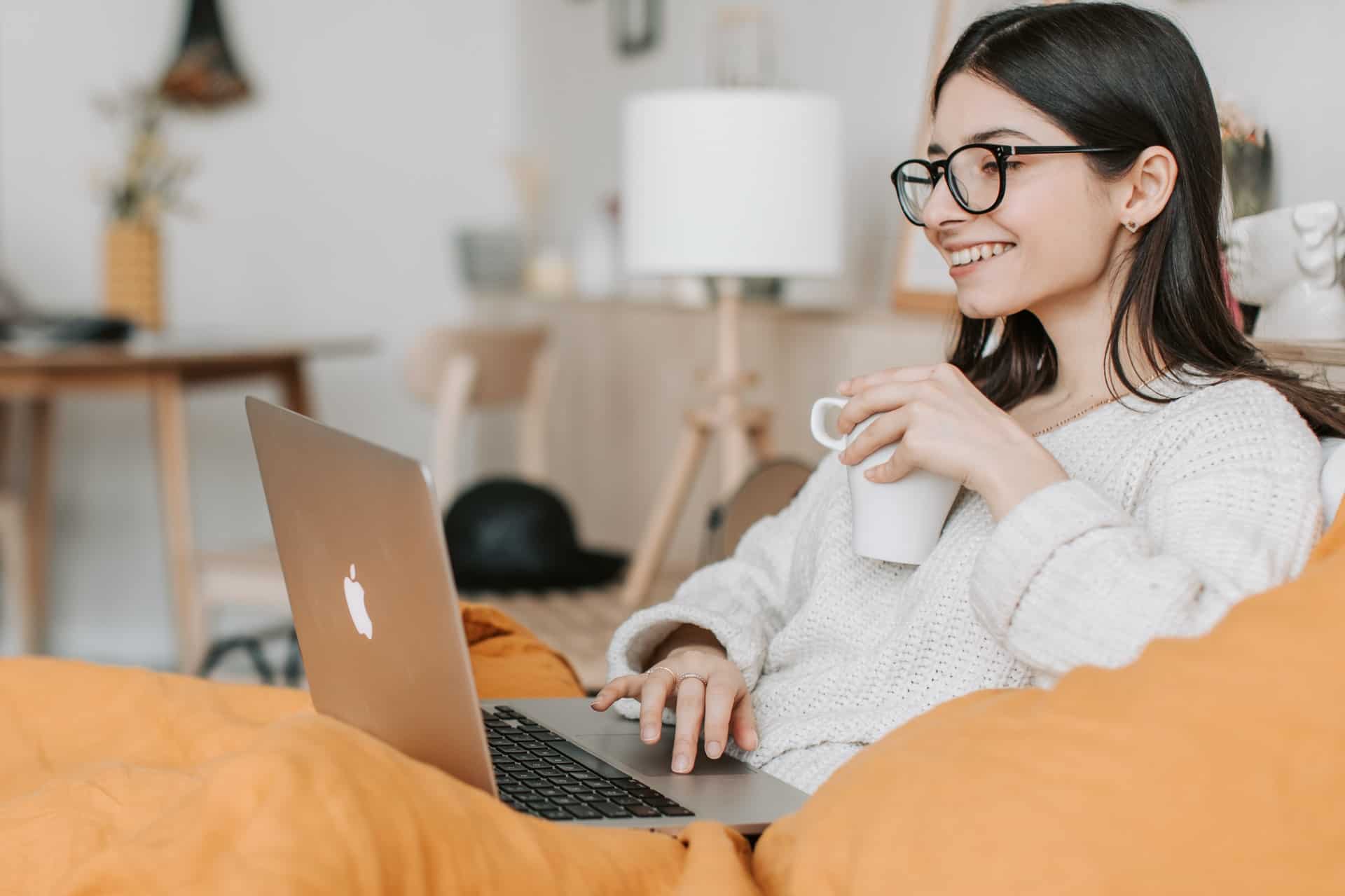 Woman smiling at laptop and drinking coffee 